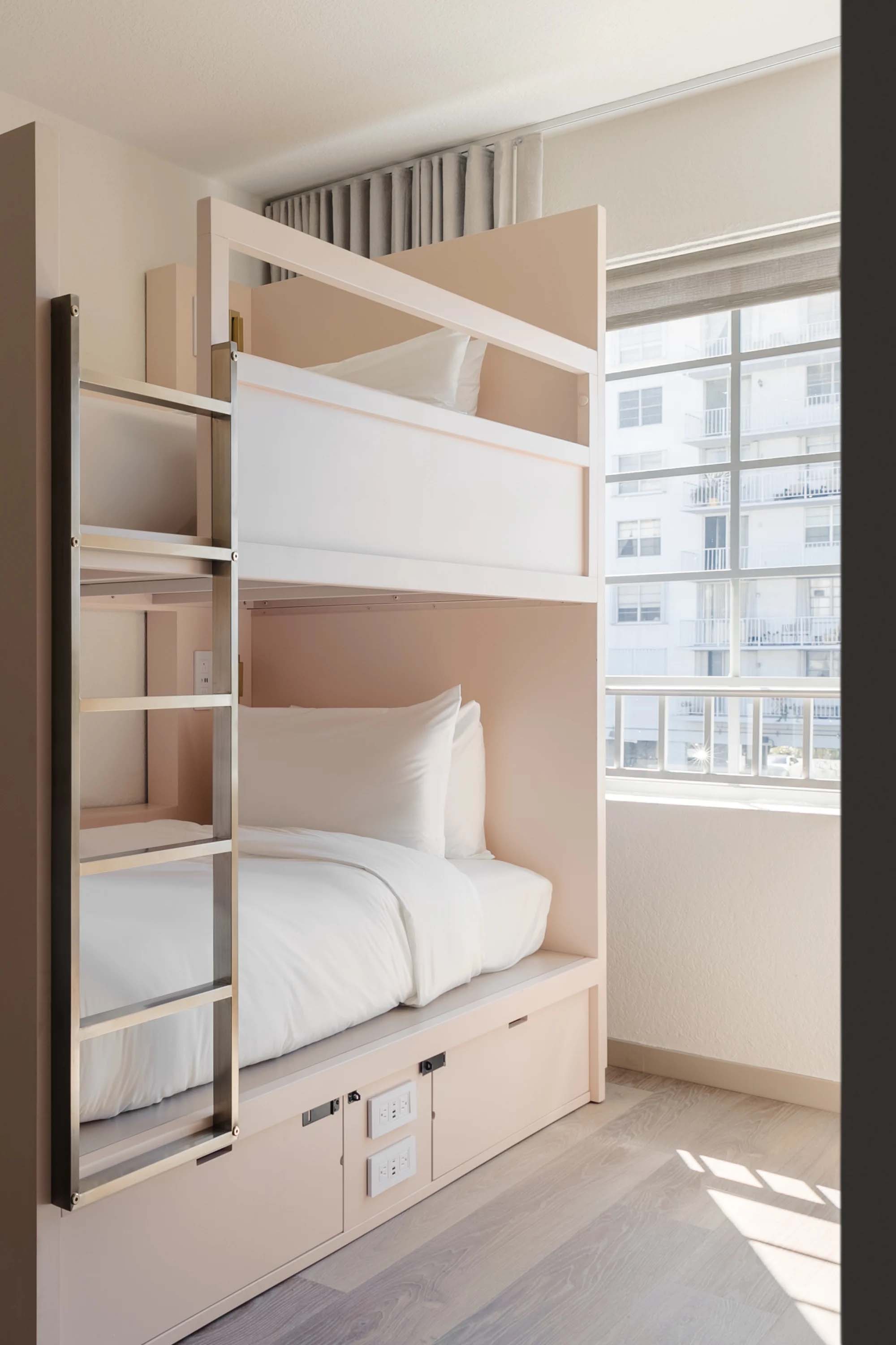 A compact room with a bunk bed, window, and wood floor.