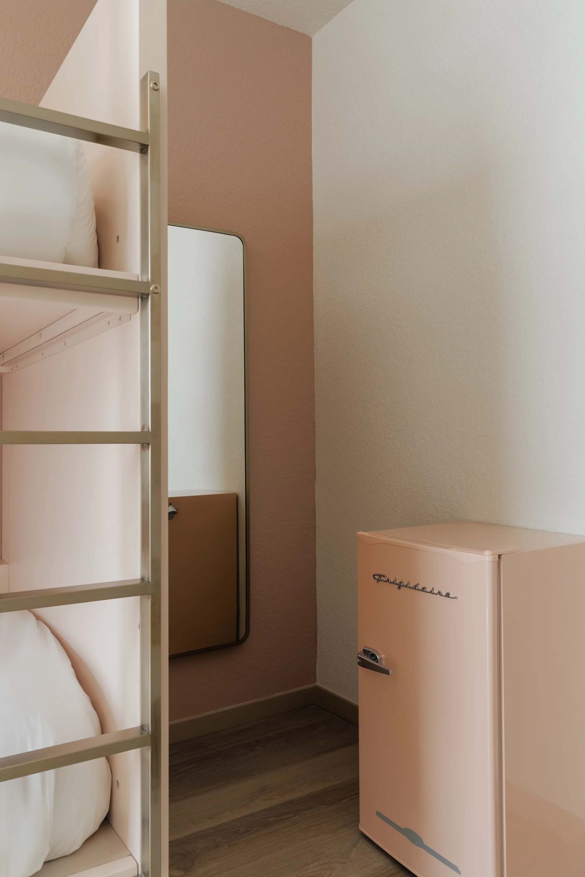 A compact room with a bunk bed, pink walls, and a small refrigerator.