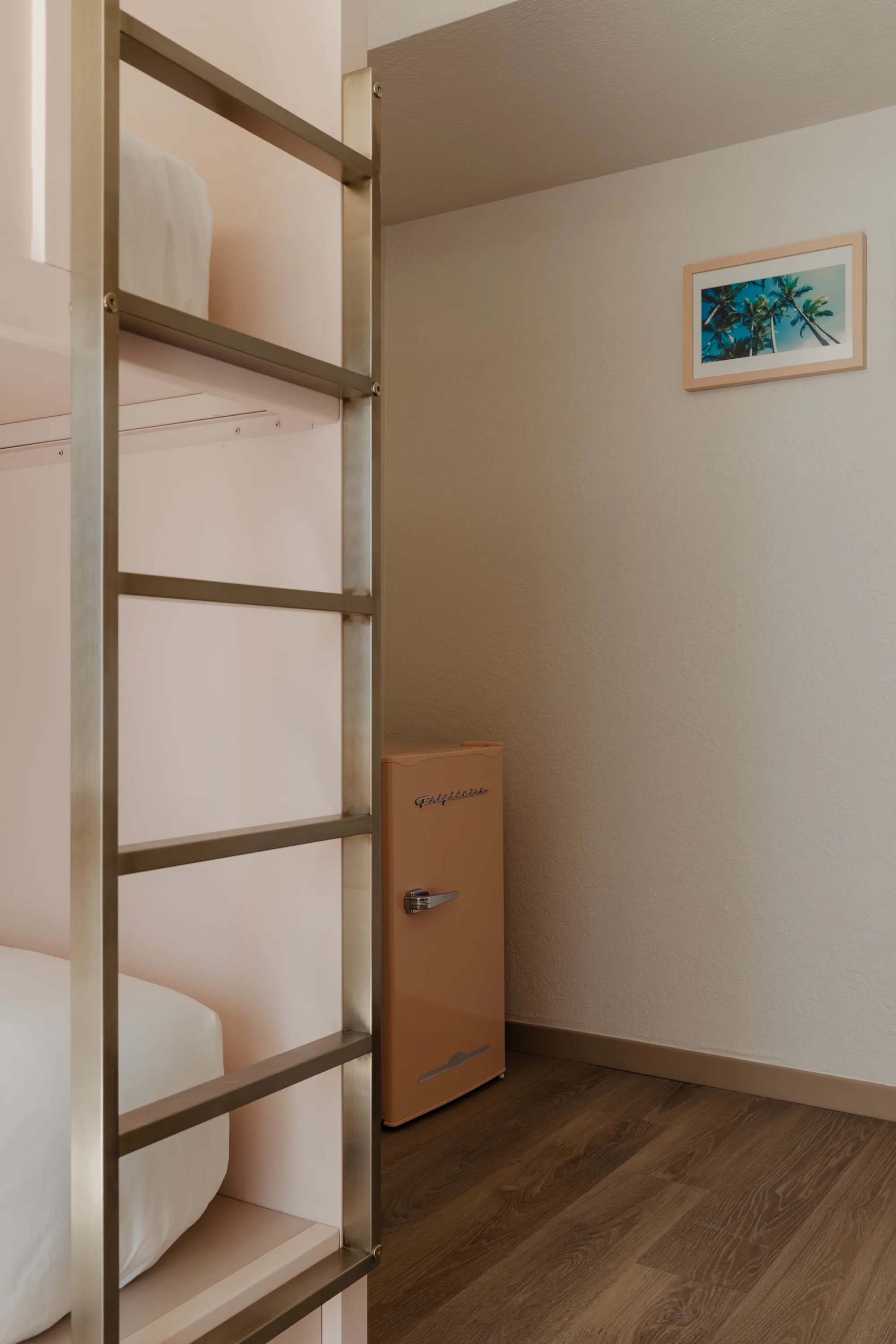 A compact room with a bunk bed, mini fridge, and wood flooring.