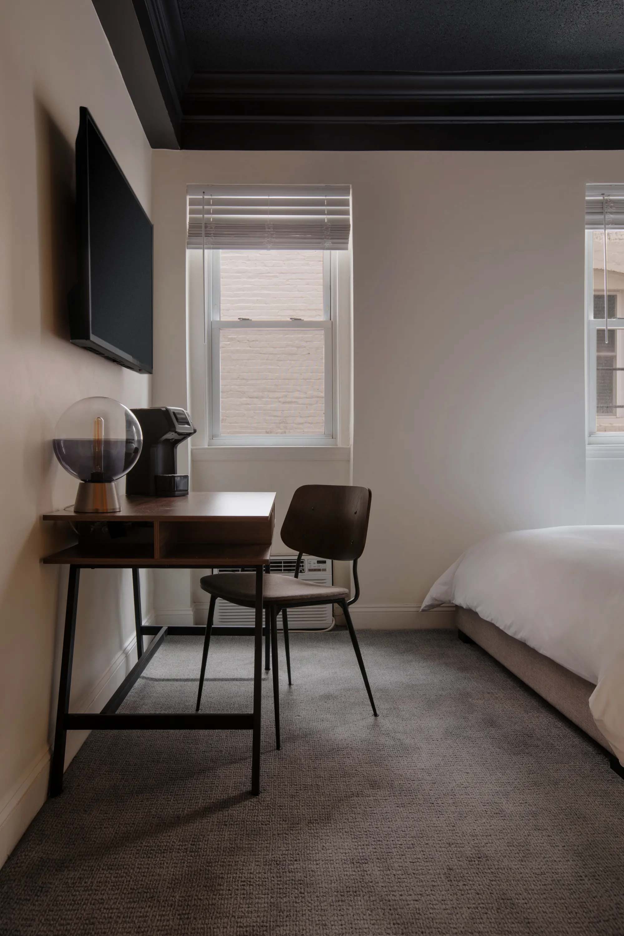 A hotel room with a desk, chair, bed, and window